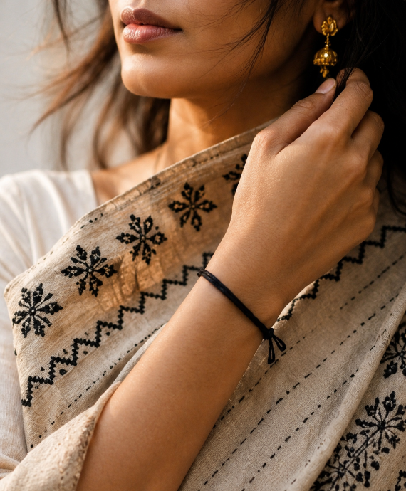 Close-up of a person wearing a beige embroidered shawl with black patterns, holding it with one hand.